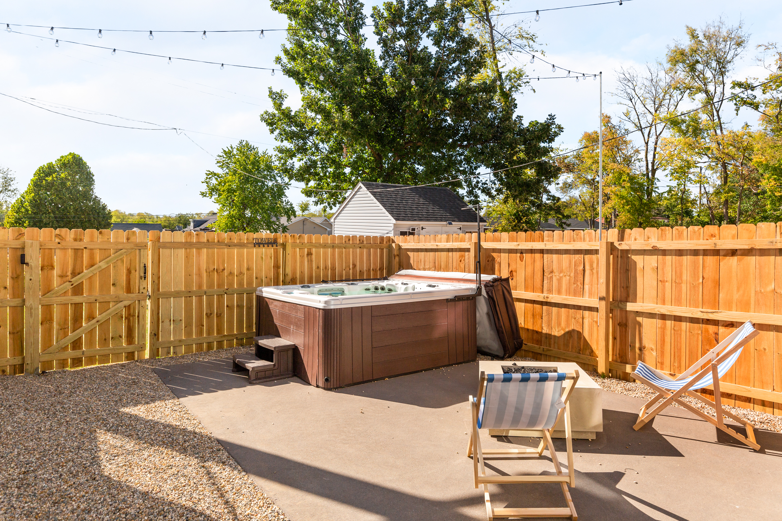 Private backyard with hot tub, lounge chairs, and string lights